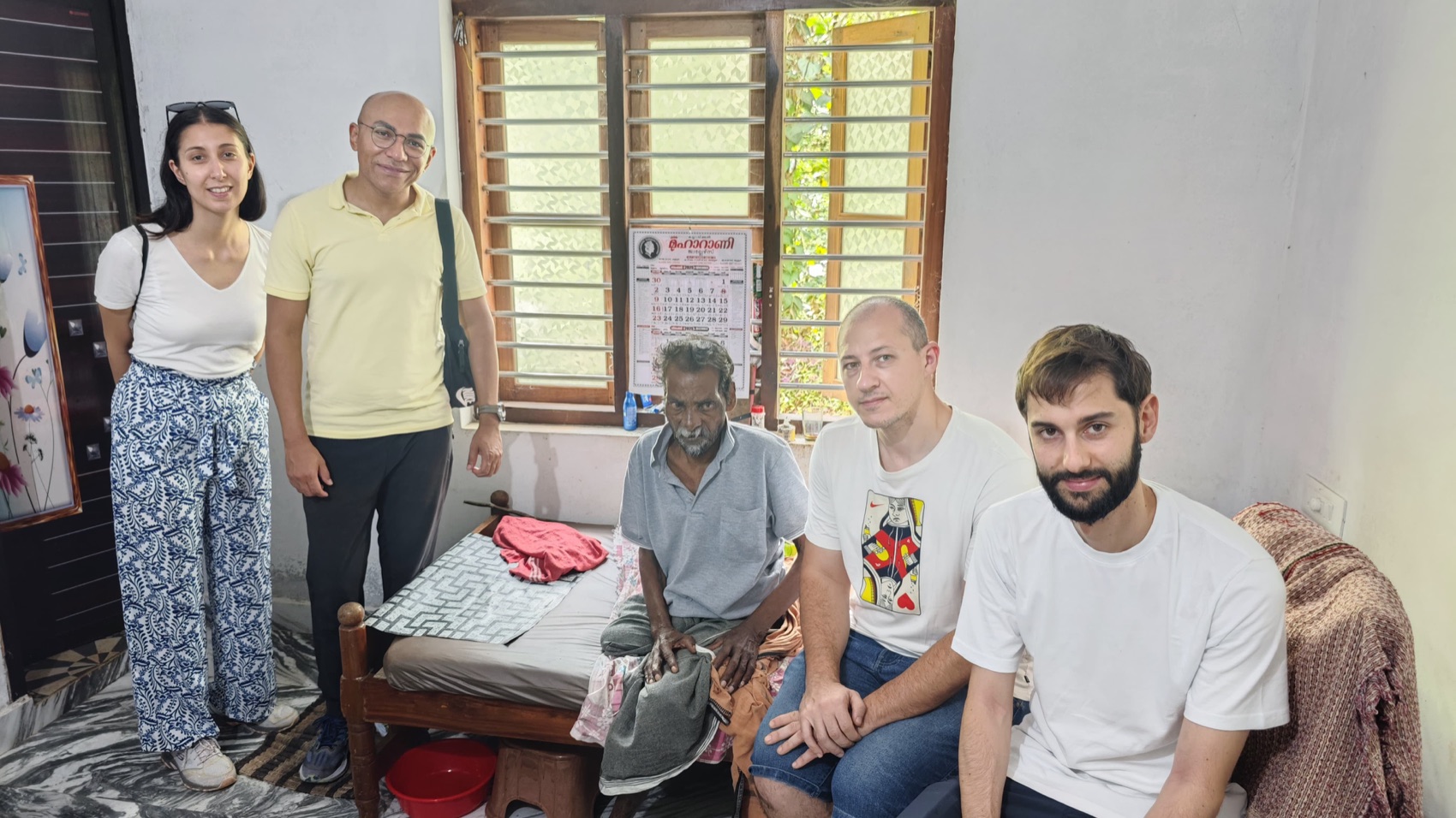 Friends and volunteers from abroad sit beside an elder on a village home visit.